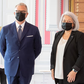 Un homme en costume et portant un masque se tient à la droite de la gouverneure générale Mary May Simon pour la prise d’une photo.