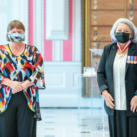 A woman who has just been given a medal stands next to Governor General Mary May Simon. Both are wearing masks.