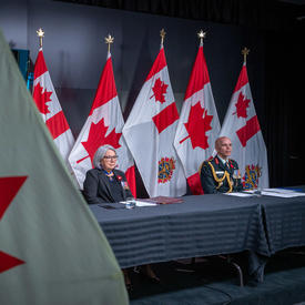 La gouverneure générale Mary Simon est assise à une longue table avec le général Wayne Eyre. Ils font tous deux face à la caméra. Derrière eux il y a des drapeaux canadiens et des Forces armées canadiennes.