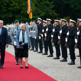 La gouverneure générale et le président de l’Allemagne marchent le long d’un tapis rouge au Schloss Bellevue. Il y a des personnes en uniforme militaire le long du tapis rouge.