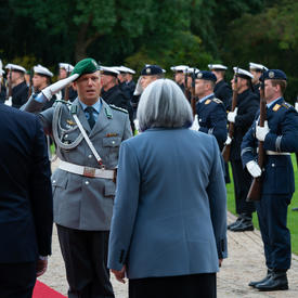 La gouverneure générale et le président de l’Allemagne marchent le long d’un tapis rouge au Schloss Bellevue. Il y a des personnes en uniforme militaire le long du tapis rouge.