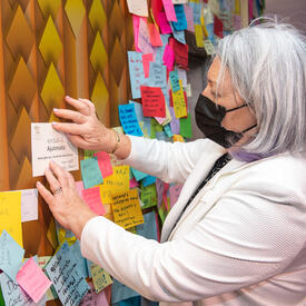 Governor General Mary Simon is sticking a piece of paper to a message board at the Ukraine Pavilion. The wall around it is covered with multi-coloured post-its.