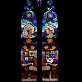 Un vitrail comportant des images de la reine Victoria et de la reine Elizabeth II, la couronne royale, leurs monogrammes et armoiries respectifs et deux représentations du Parlement du Canada.