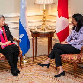 Governor General Mary Simon is pictured speaking to a woman. The Quebec flag and the Canadian flag are in the background. 