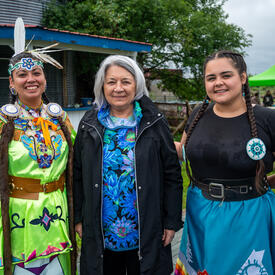 Governor General Simon is standing between two women at Mādahòkì Farm. They are outside and smiling.