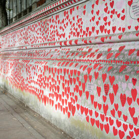 Thousands of small red hearts with printed messages are painted on a concrete wall. 