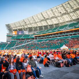 A group of students wearing orange shirts are standing on the floor of a stadium.
