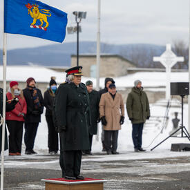 La gouverneure générale est debout à l'extérieur sur un petit podium. Le drapeau du gouverneur général est suspendu à un mât à sa droite.