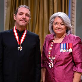 La gouverneure générale Simon se tient à côté d’un homme qui porte une médaille autour du cou.
