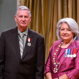 La gouverneure générale Simon se tient à côté d’un homme qui porte une médaille épinglée à son blazer noir.