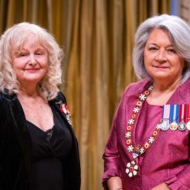 La gouverneure générale Simon se tient à côté d’une femme qui porte une médaille épinglée à son blazer noir.