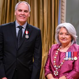 La gouverneure générale Simon se tient à côté d’un homme qui porte une médaille épinglée à son blazer noir.