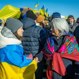 La gouverneure générale Mary Simon parle à une femme qui s’est enveloppée dans un drapeau ukrainien. Une grande foule se trouve derrière elles. De nombreuses personnes dans la foule tiennent des drapeaux ukrainiens.