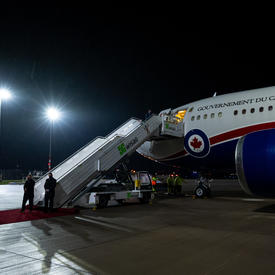 L'avion du gouvernement du Canada est sur le tarmac de l'aéroport. La porte de l'avion est ouverte et les escaliers sont ouverts en attendant que les passagers descendent. 