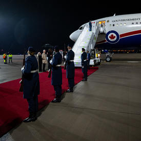 L'avion du gouvernement du Canada est sur le tarmac de l'aéroport. La porte de l'avion est ouverte et les escaliers sont ouverts en attendant que les passagers descendent. Il y a un tapis rouge à la base de l'avion.