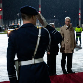 Un homme en uniforme salue un fonctionnaire du gouvernement allemand. Ils sont dehors, debout sur le tapis rouge sur le tarmac de l'aéroport.