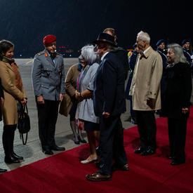 La gouverneure générale Mary Simon et Monsieur Whit Grant Fraser sont accueillis par des représentants allemands et canadiens. Ils sont sur un tapis rouge au pied d’un avion. Des personnes en uniforme militaire sont debout le long du tapis rouge.
