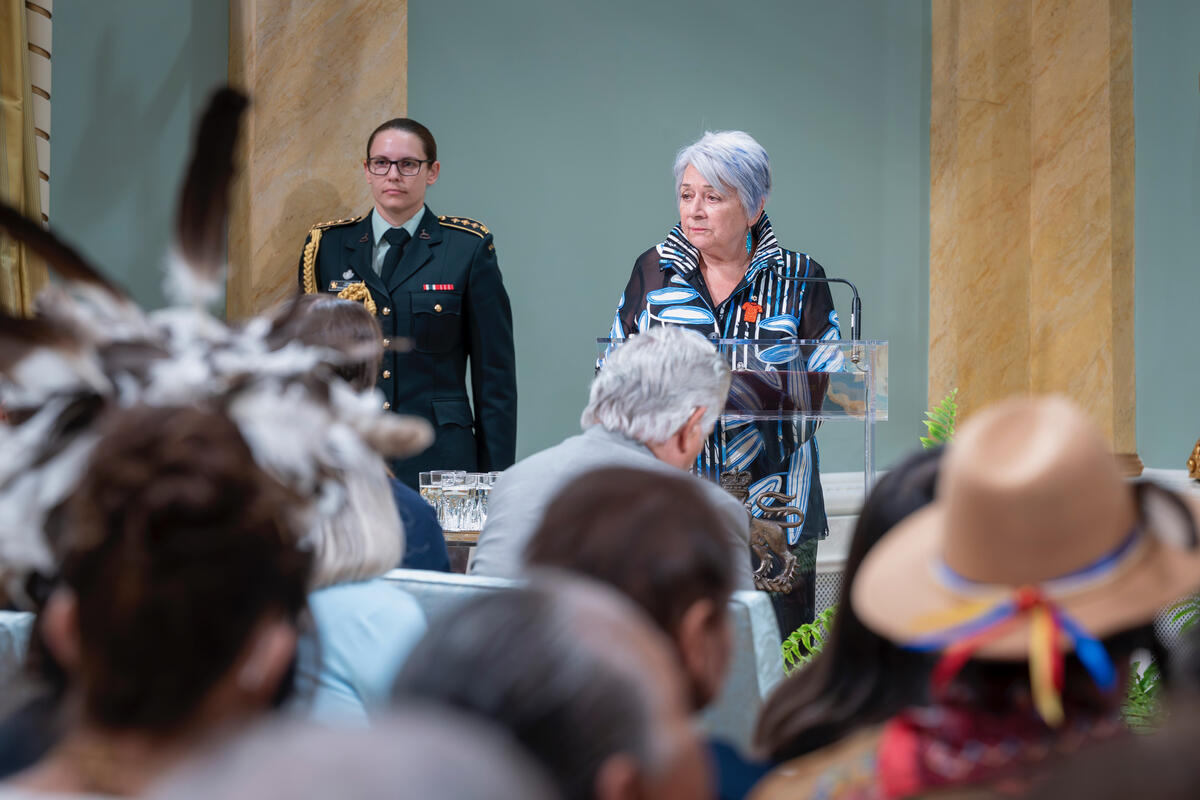 A silver haired woman at a podium in front of a crowd