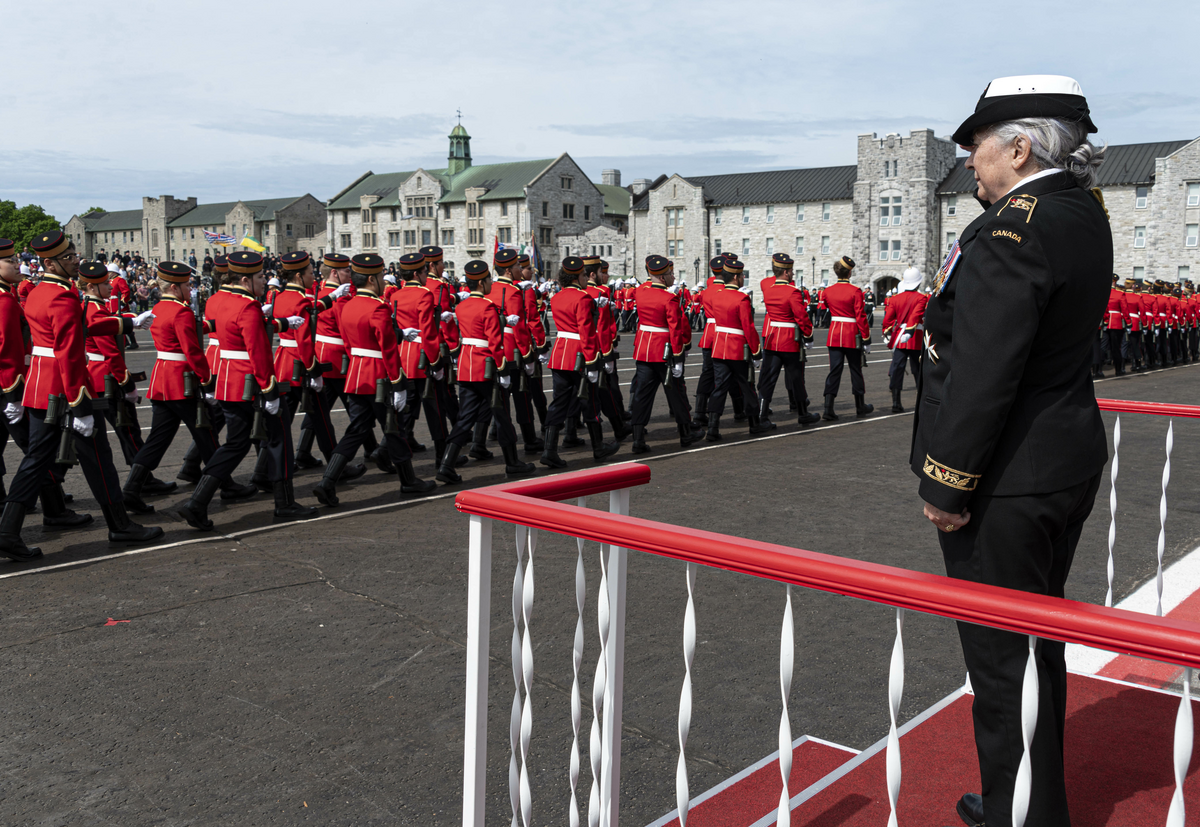 La gouverneure générale debout sur une petite plateforme, tandis que des cadets en uniforme passent devant elle. 