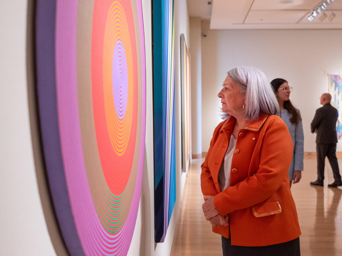 La gouverneure générale Simon inspecte une œuvre d'art colorée accrochée à un mur.