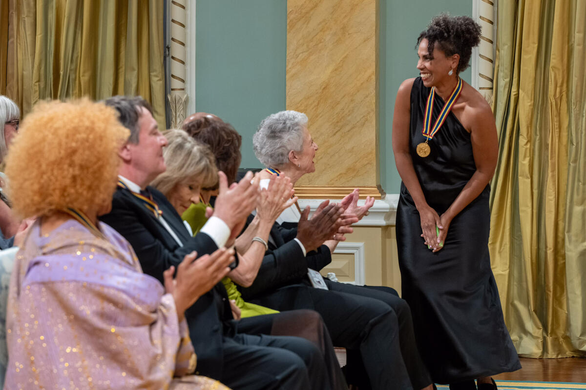 Mélanie Demers se lève et sourit pendant que le public l'applaudit dans la salle de bal de Rideau Hall