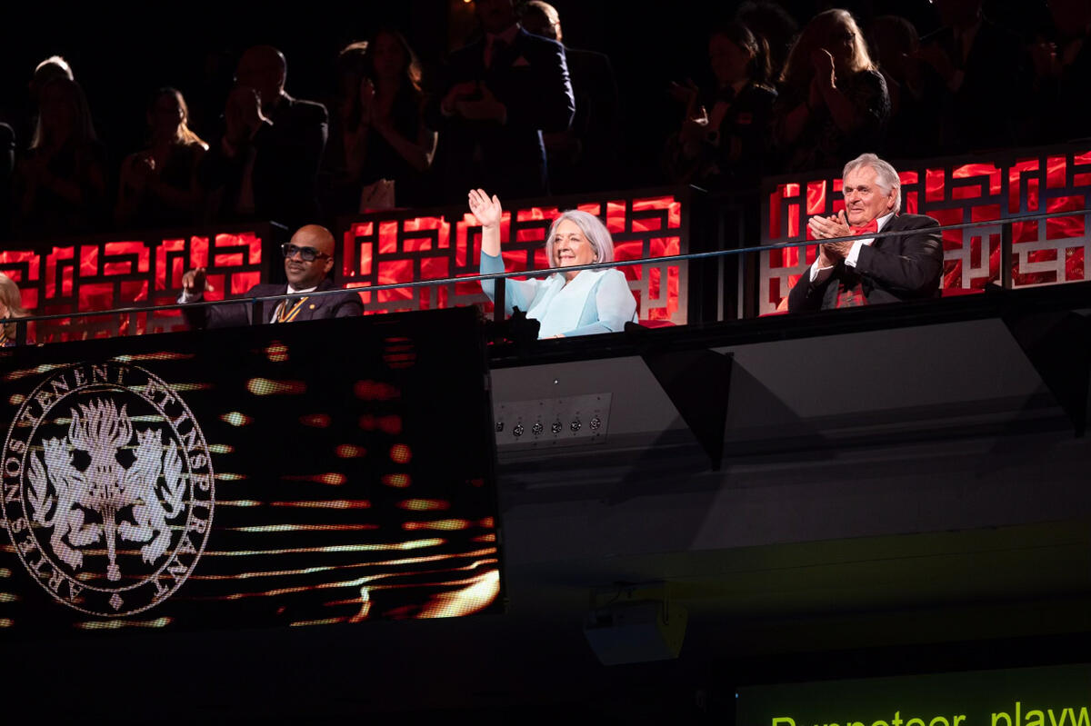 La gouverneure générale Mary Simon salue le public, assis à côté de M. Whit Fraser et de Wes « Maestro » Williams. Le logo du gala est visible sur un écran devant eux.