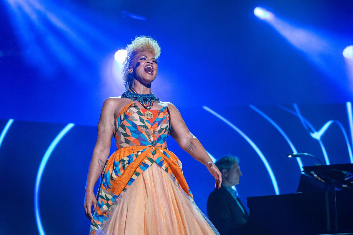 Une chanteuse chante tandis qu'un pianiste joue du piano en arrière-plan. L’arrière-plan est allumé avec des lumières bleu.