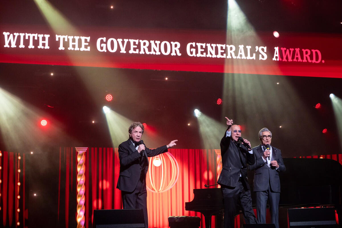 M. Martin Short, M. Eugene Levy et M. Paul Shaffer chantent une pièce musicale. Les mots « …avec le Prix du Gouverneur général ». peut être vu au-dessus d’eux.