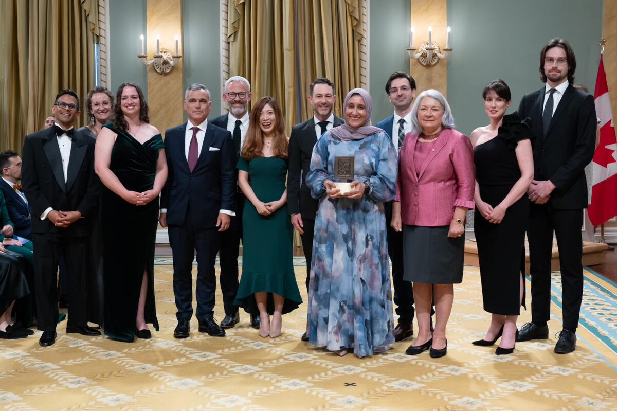 Un groupe de personnes debout. Une femme au milieu tient un trophée. Le groupe pose pour une photo.