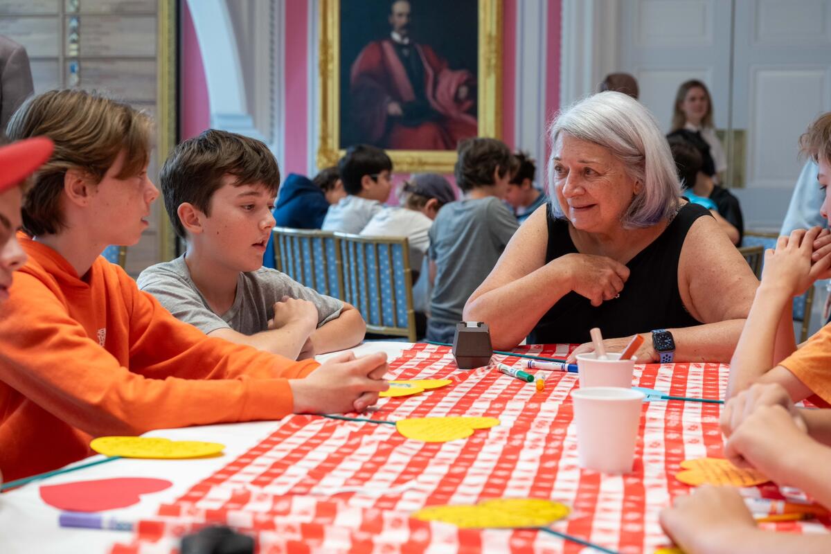 La gouverneure générale Mary Simon est assise à une table avec des enfants. Il y a des marqueurs et du carton en forme de cœur découpé sur la table.