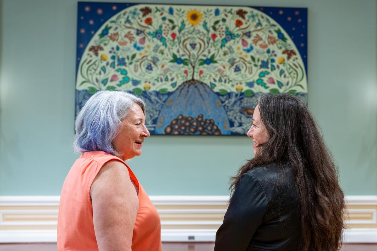 Governor General Mary Simon and a woman are looking at each other. There is a large painting on the wall behind them.