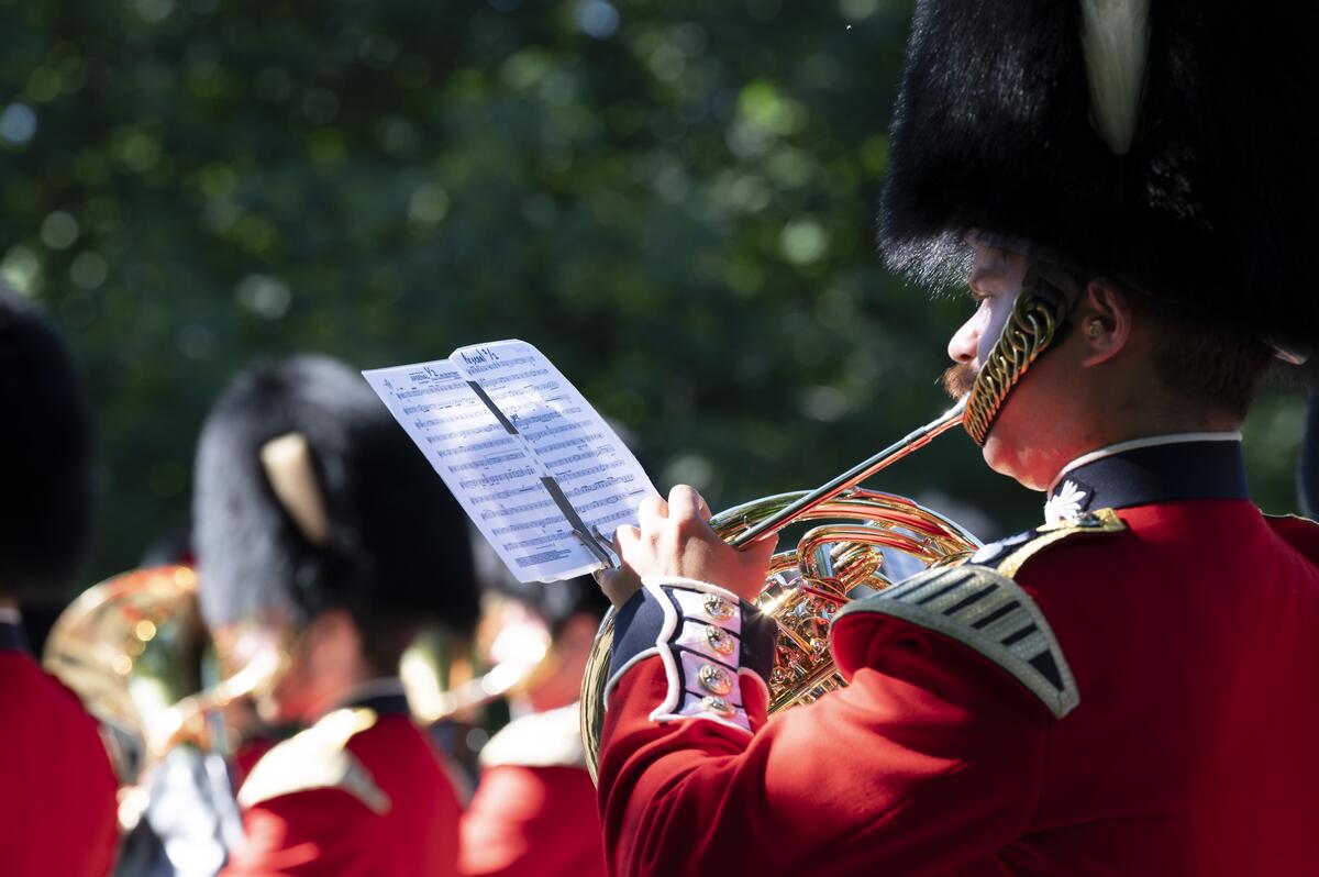 Un membre des Forces armées canadiennes joue du cor français. Il porte un uniforme rouge.