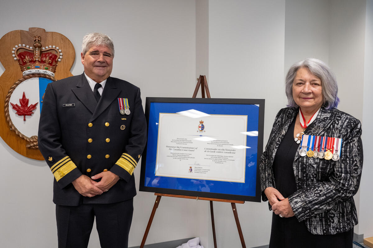 Governor General Simon posing next to a man in uniform. There is a framed certificate on an easel between them.
