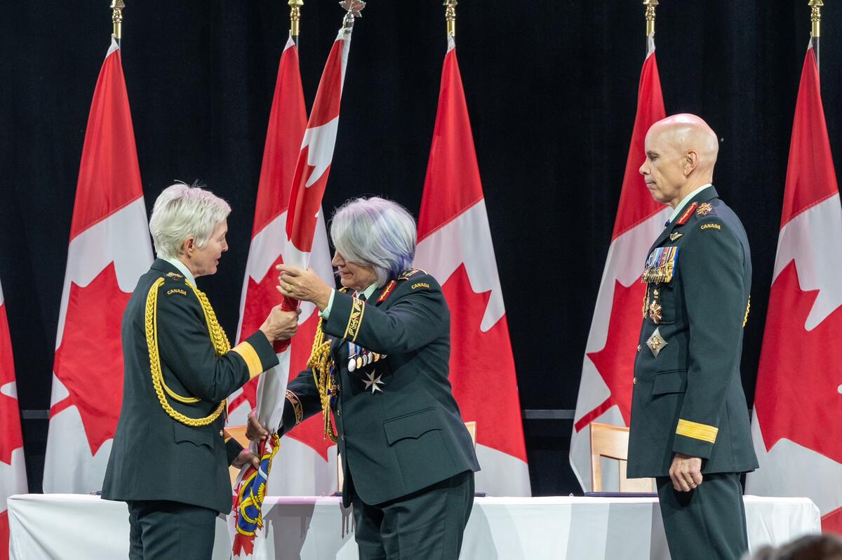 La gouverneure générale Mary Simon remet le pavillon des Forces armées canadiennes au général Jennie Carignan. Le général Wayne Eyre se tient derrière elle.