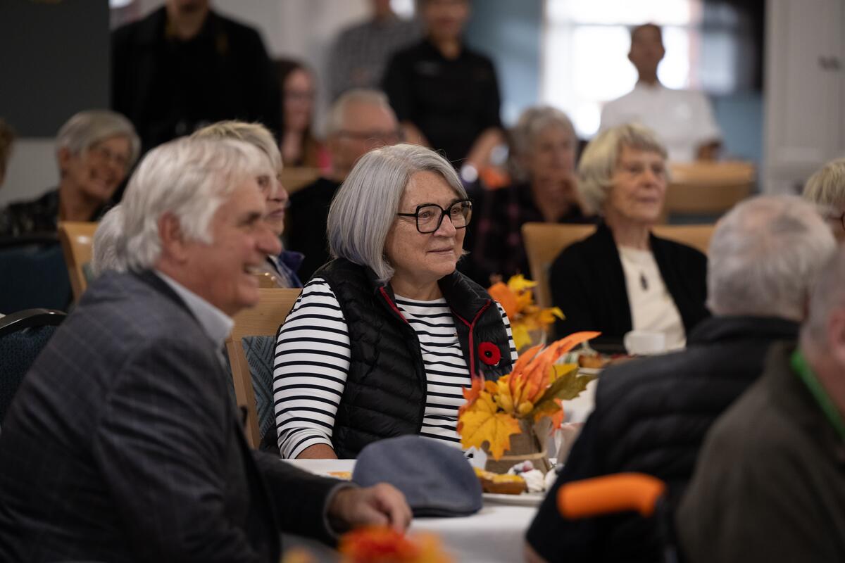 La gouverneure générale et M. Whit Fraser, le sourire aux lèvres, sont assis au milieu d'un groupe de personnes.