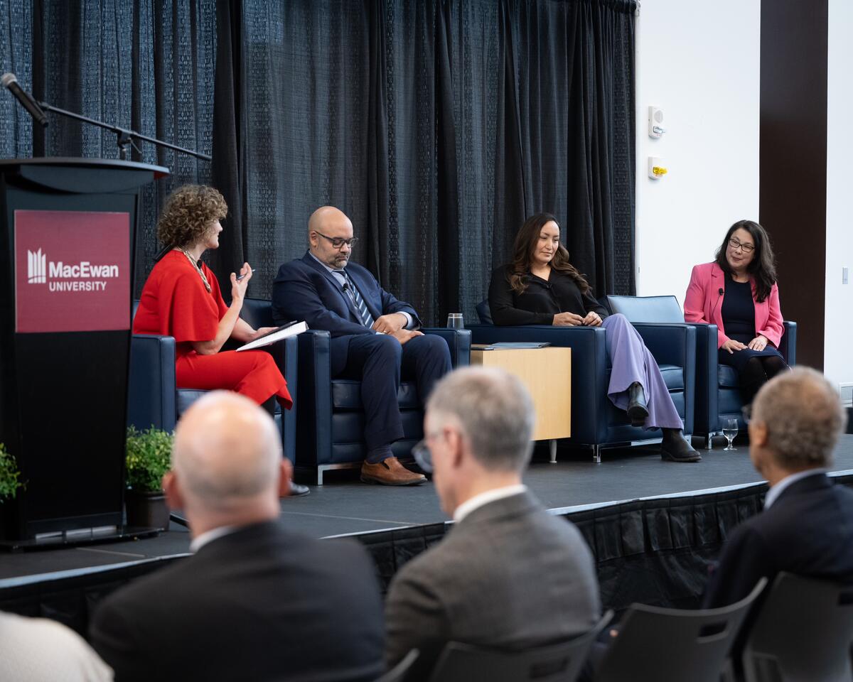 Un groupe de quatre personnes se trouve assis sur une scène et s'adresse à la foule.
