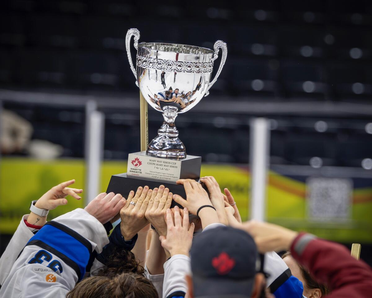 Several hands hoisting a ringette cup in the air.