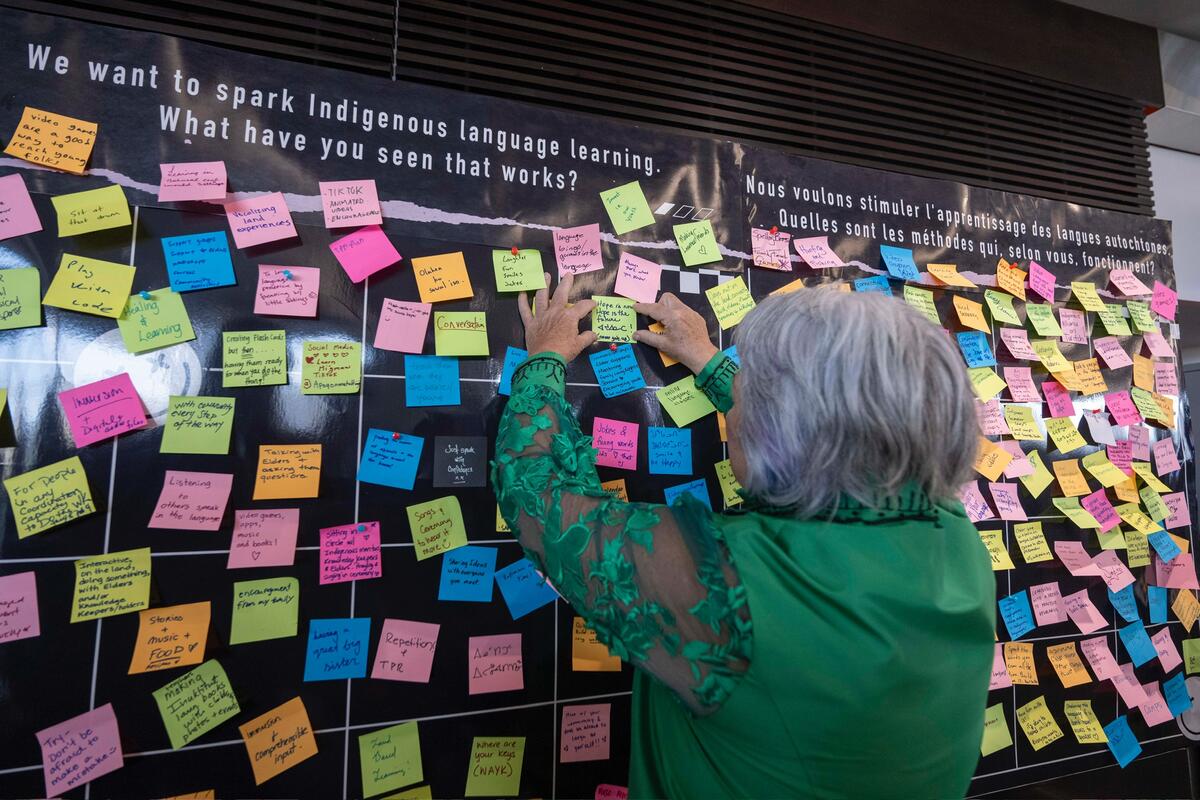 Woman adding a post-it note to a wall filled with colourful messages.