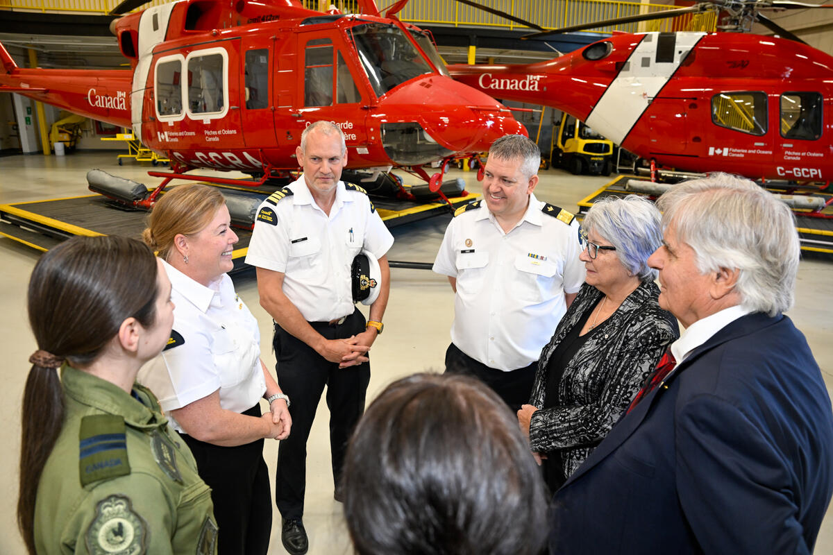La gouverneure générale Simon et M. Whit Fraser discutent avec des membres de la Garde côtière canadienne. Deux hélicoptères rouges sont visibles à l'arrière-plan.