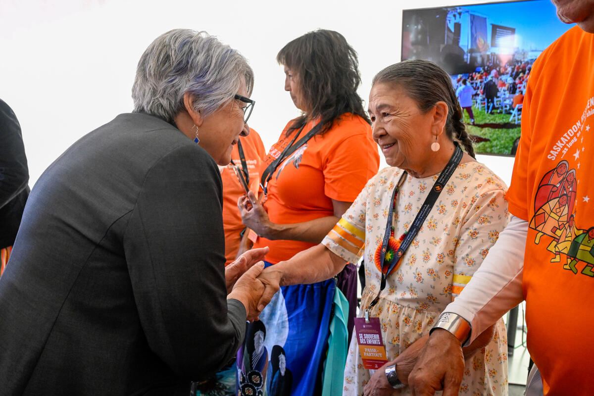 Governor General Mary Simon shaking hands with a person. Other people are standing nearby dressed in orange shirts.