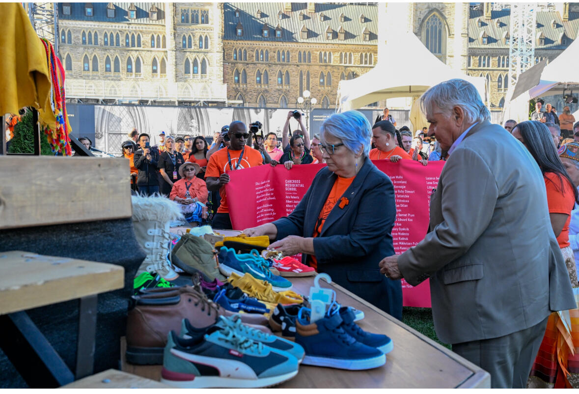 Governor General Mary Simon and Mr. Whit Fraser placing shoes on a stage at an event for National Day for Truth and Reconciliaton.