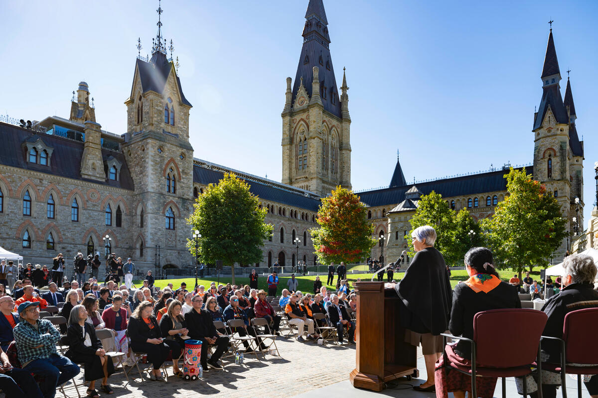 Governor General Mary Simon standing at a podium, speaking to a crowd of people outside of Parliament.