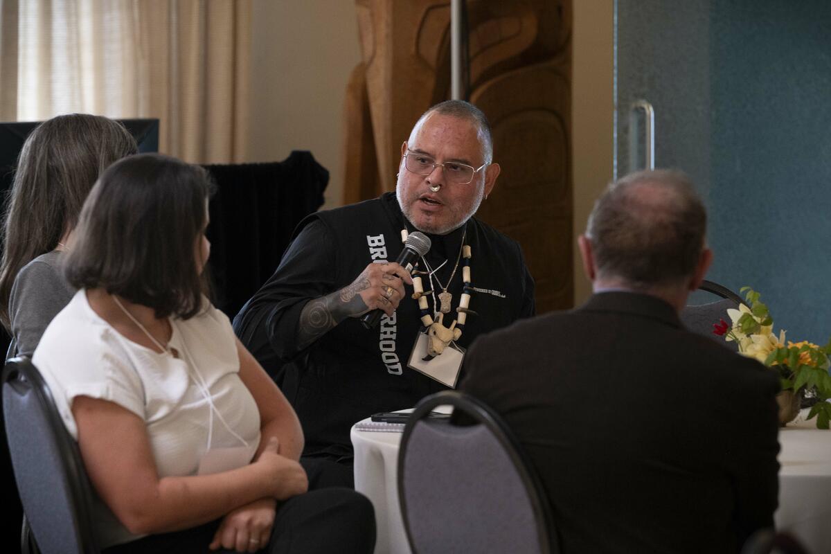 Des personnes assises à une table. Une personne tient un micro.