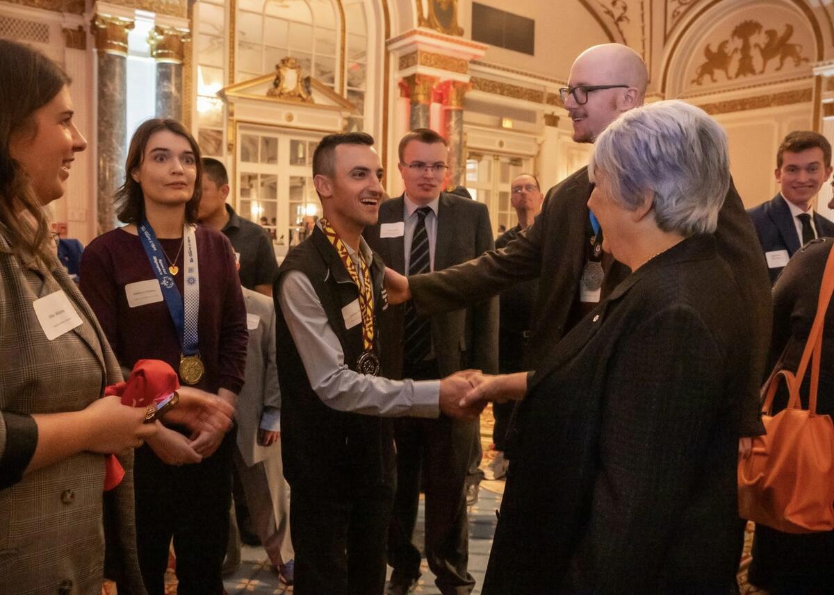 Governor General Mary Simon shaking hands with a person. Others are standing with them. Some are wearing medals.