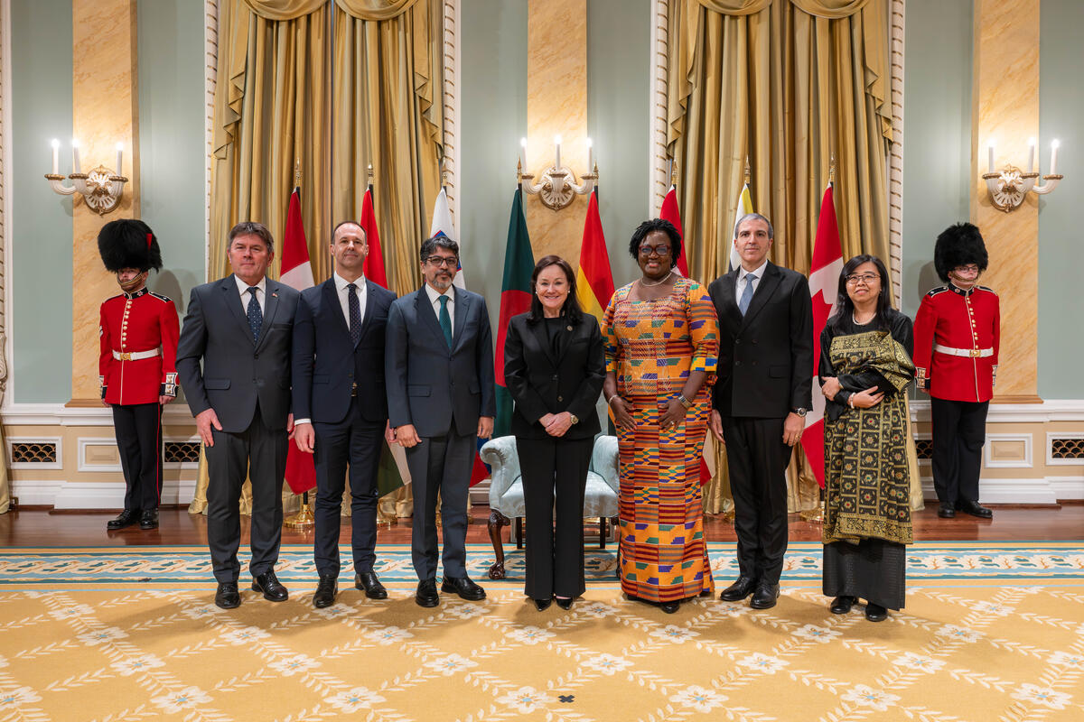 A group photo with the Honourable Suzanne Côté and six new heads of mission, with the flags of each country behind them. Two Ceremonial Guards are in the back.