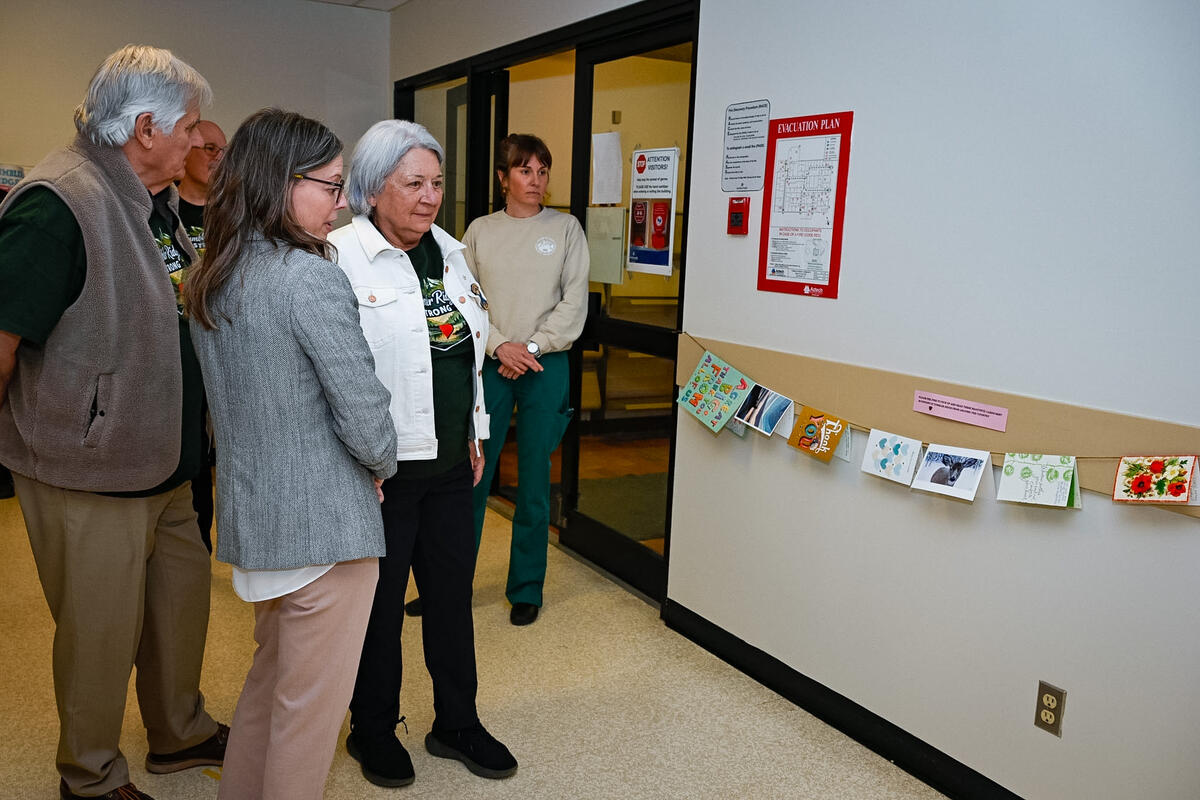 Governor General Mary Simon and Mr. Whit Fraser being shown a row of cards strung together on a wall.