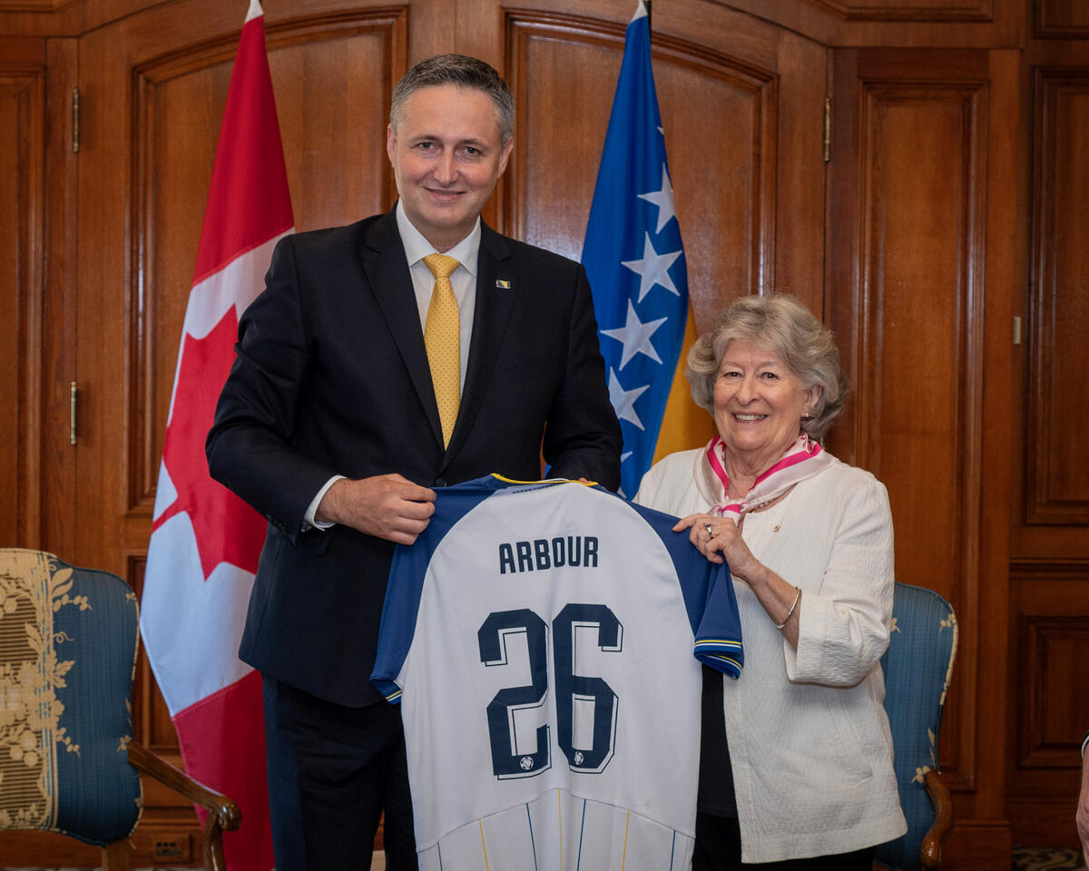 Governor General Louise Arbour standing next to His Excellency Denis Bećirović, Chairman of the Presidency of Bosnia and Herzegovina. She is holding up a white jersey with the name 'Arbour' and the number 26 on it.