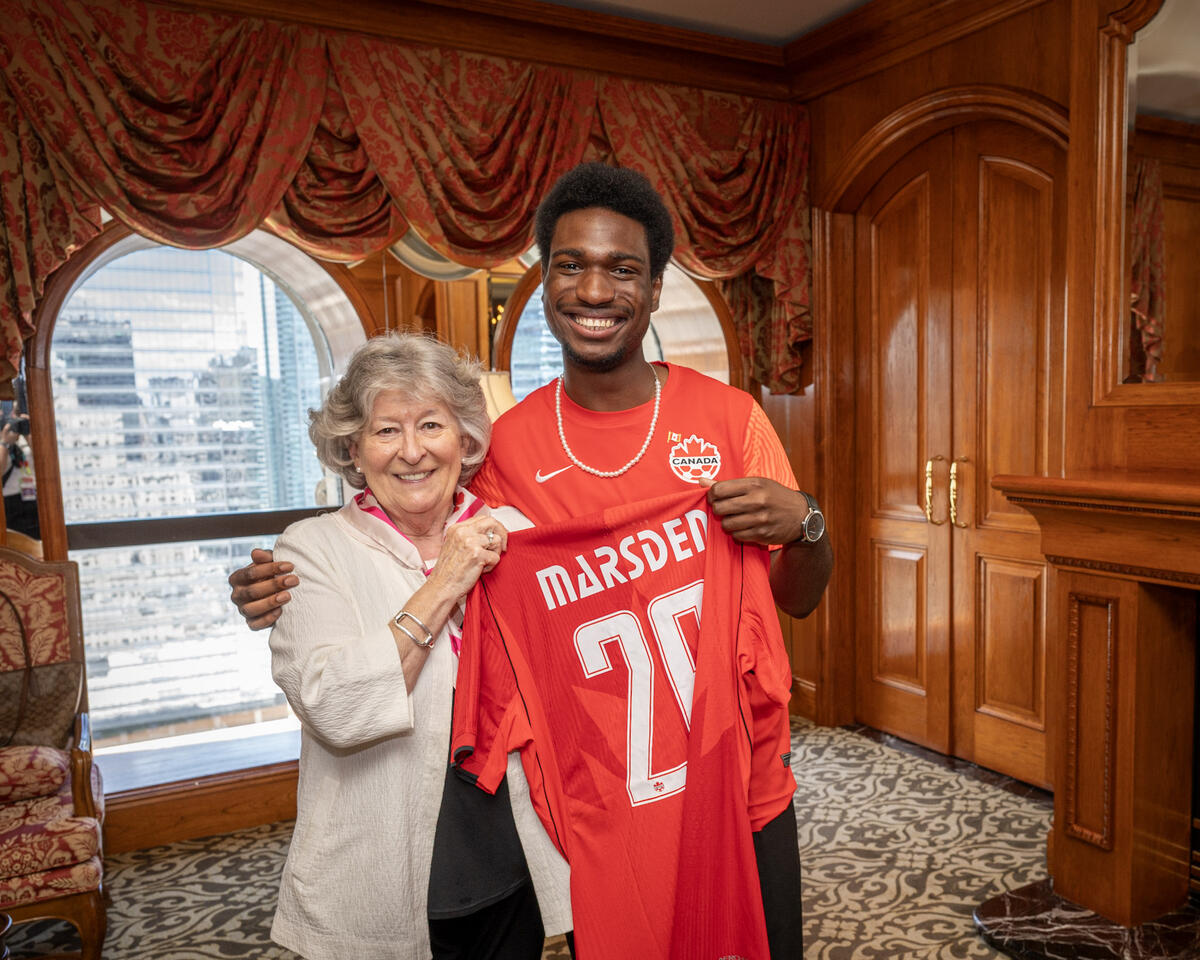 Governor General Louise Arbour standing next to a secondary school student. They are both holding a red jersey with the name "Marsden" on it, and the number 26.