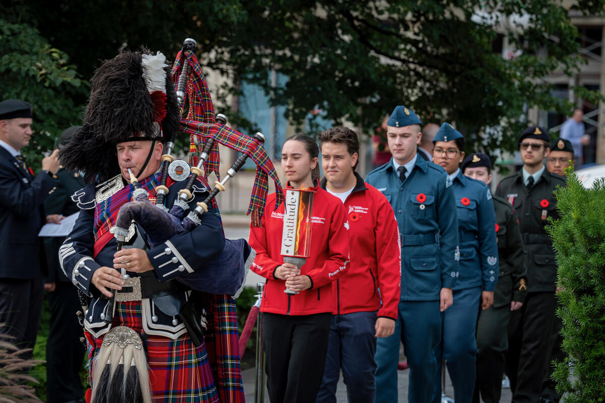Une file de personnes en uniforme marchant derrière une personne qui joue de la cornemuse.