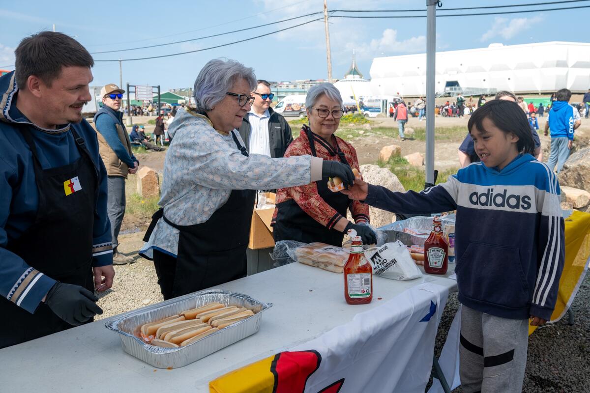 La gouverneure générale Mary Simon sert un hot-dog à un jeune visiteur lors des célébrations de la Journée du Nunavut.